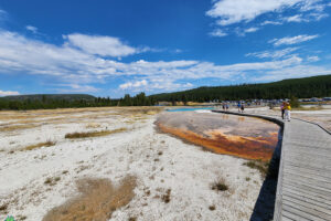 Looking back at Black Diamond Pool and the parking area as we hike on around the loop at Biscuit Basin Yellowstone National Park with Get Lost in America your Yellowstone Cabin rentals experts